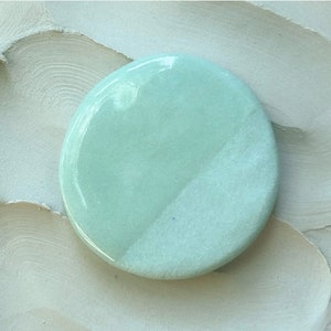 May include: A round, light green ceramic tile with a white glaze on one half. The tile is smooth and glossy.