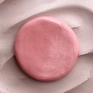 May include: A round, pink, smooth, and shiny object on a textured, light brown surface.