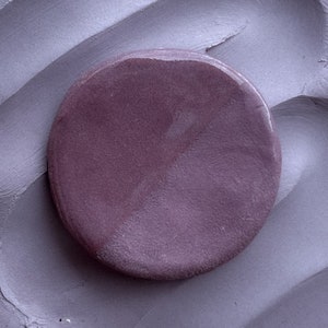 May include: A close-up of a round, purple clay disc with a textured surface.