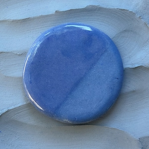 May include: A round, light blue ceramic tile with a subtle swirl pattern. The tile has a glossy finish.