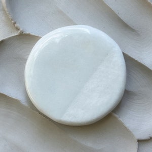 May include: A white ceramic dish with a smooth, glossy finish. The dish is round and has a slightly raised edge.