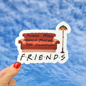 May include: A white sticker with a brown couch, a lamp, and the words "FRIENDS" with dots between each letter. The couch has the names "Phoebe, Ross, Monica, Rachel, Joey, Chandler" written on it.