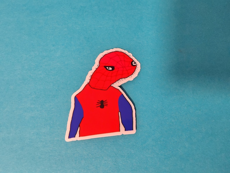 Puede incluir: Una pegatina de dibujos animados roja y azul de una persona con un disfraz de Spiderman. La persona tiene una cabeza grande y un cuerpo peque&ntilde;o. La pegatina est&aacute; sobre un fondo azul.
