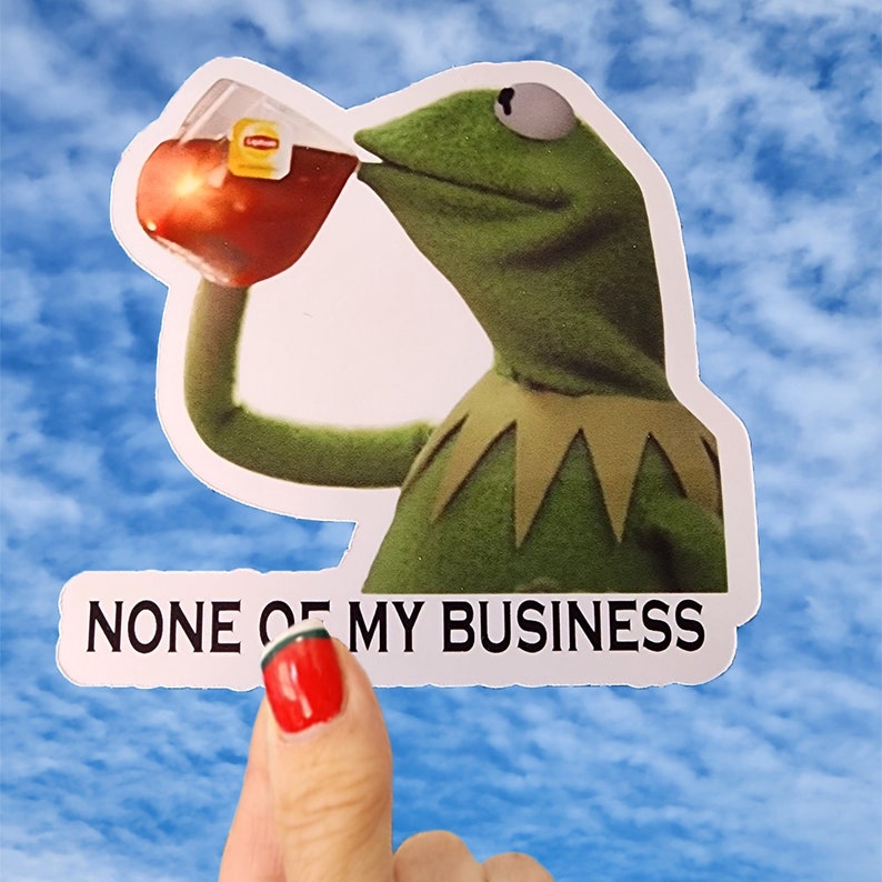 May include: A green frog sticker with a yellow collar, drinking from a red cup. The sticker has the text "NONE OF MY BUSINESS" printed on it.