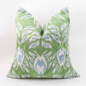 May include: A square cushion featuring a green background with a repeating pattern of blue and white leaf-like shapes. The cushion is made of a soft, textured fabric.
