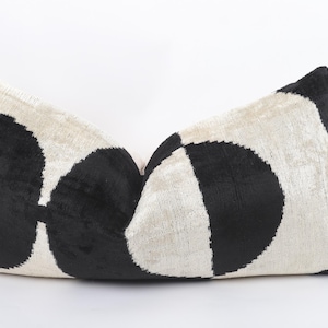 Könnte beinhalten: Ein dekoratives rechteckiges Kissen mit cremefarbenem Hintergrund und großen, schwarzen, kreisförmigen Mustern. Das Kissen hat ein weiches, strukturiertes Aussehen und ist für die Inneneinrichtung konzipiert. Das Kissen ist rechteckig.