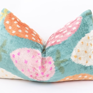 May include: Decorative throw pillow with a teal background and a repeating pattern of stylized strawberries in orange, pink, and white. The strawberries have white dotted accents and green stems. The pillow is made of a soft, textured fabric.