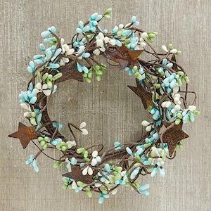 May include: A circular wreath constructed from thin brown twigs, adorned with small light blue, white, and pale green berries. Several flat, five-pointed stars with a rusted, dark brown metal finish are interspersed throughout the berry clusters.