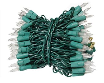 May include: A coiled strand of clear incandescent string lights featuring a dark green wire and green plastic bulb sockets. The set includes a standard two-prong electrical plug at one end, with multiple small, transparent glass bulbs attached.