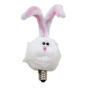 May include: A decorative light bulb shaped like a white rabbit head with long, upright ears featuring pink centers. The rabbit has small black eyes, a tiny pink nose, and a metallic screw-in base at the bottom, designed for use in a standard light fixture.