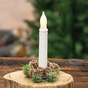May include: A white, battery-operated candle with a flickering flame effect, surrounded by a wreath of pinecones and greenery. The candle sits on a wooden base, creating a rustic, festive display. Perfect for holiday decor.