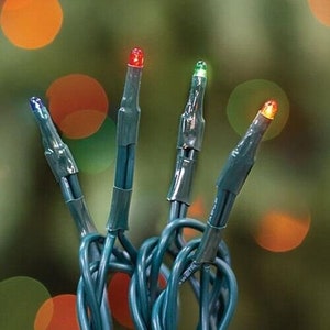May include: Close-up of a string of Christmas lights with four multi-colored bulbs. The bulbs are blue, red, green, and orange. The wires are green and looped together. The background is a blurred green and orange.