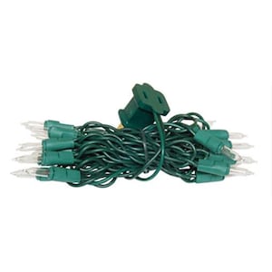 May include: A string of clear incandescent mini lights featuring a dark green wire and matching green bulb sockets. The strand is coiled into a compact bundle and includes a standard two-prong electrical plug at the top for power connection.