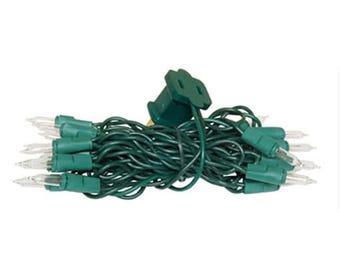 May include: A string of clear incandescent mini lights featuring a dark green wire and matching green bulb sockets. The strand is coiled into a compact bundle and includes a standard two-prong electrical plug at the top for power connection.