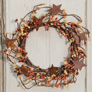 May include: A small, rustic wreath with brown twigs and orange and yellow berries. The wreath is decorated with rusty metal stars.