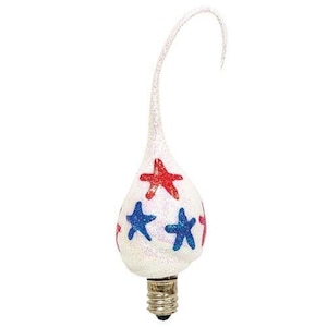 May include: A teardrop-shaped light bulb with a white glittery finish, featuring red and blue glitter star patterns. The bulb has a curved, elongated tip and a standard metal screw base at the bottom, designed for decorative lighting fixtures.