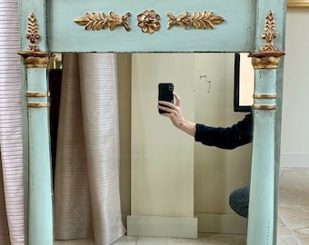 Puede incluir: Un espejo antiguo y ornamentado con un remate de águila dorada y un marco azul pálido. El espejo es rectangular y está decorado con detalles en pan de oro.