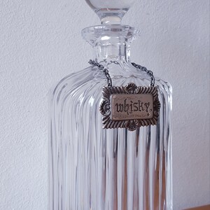 Puede incluir: Una decantador de vidrio transparente con un dise&ntilde;o acanalado y un tap&oacute;n de plata. La decantador tiene una etiqueta de plata que dice "Whisky."