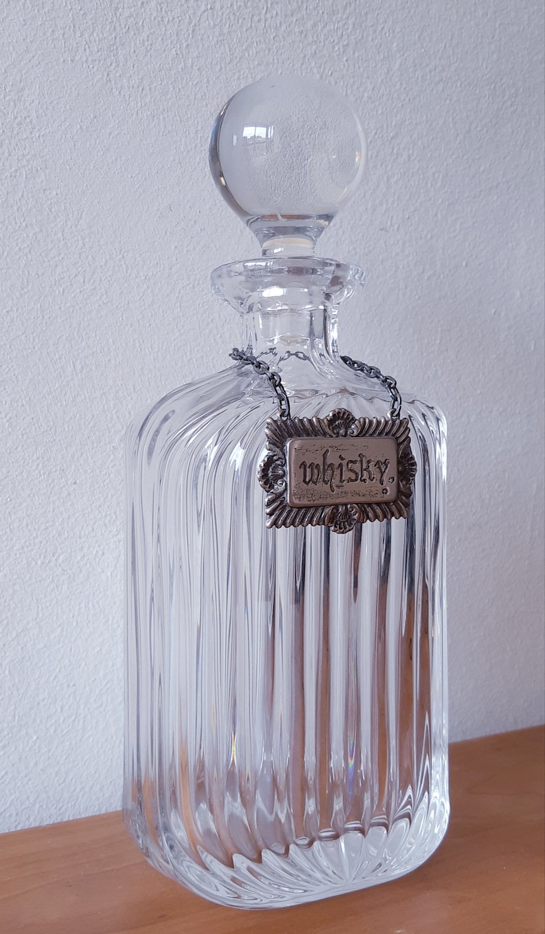 Puede incluir: Una decantador de vidrio transparente con un dise&ntilde;o acanalado y un tap&oacute;n de plata. La decantador tiene una etiqueta de plata que dice "Whisky."