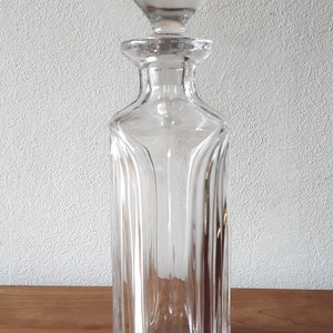 Puede incluir: Una decantador de vidrio transparente con un tap&oacute;n redondo. La decantador tiene un cuerpo cuadrado con nervaduras verticales.