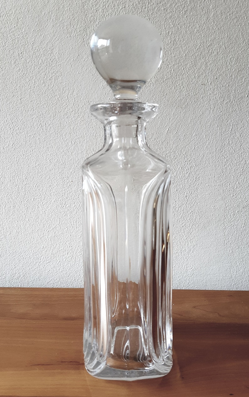 Puede incluir: Una decantador de vidrio transparente con un tap&oacute;n redondo. La decantador tiene un cuerpo cuadrado con nervaduras verticales.