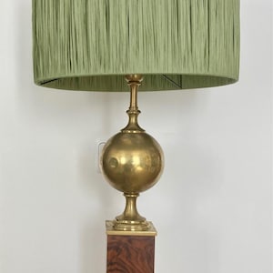 Puede incluir: Una lámpara de mesa de latón con una pantalla de lámpara plisada verde. La lámpara tiene una base redonda y una base cuadrada de madera.