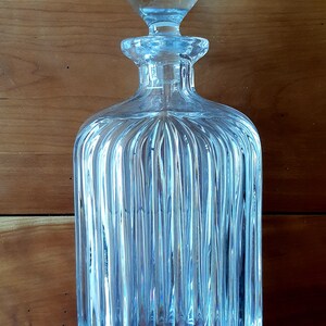 Puede incluir: Una decantador de vidrio transparente con un dise&ntilde;o acanalado y un tap&oacute;n redondo. La decantador est&aacute; vac&iacute;a y tiene un tono azul claro.