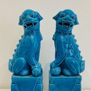 Può includere: Una coppia di cani foo in ceramica turchese, leoni guardiani tradizionali cinesi, seduti su basi quadrate. I cani foo sono dettagliati con intricate sculture e hanno un'espressione feroce.