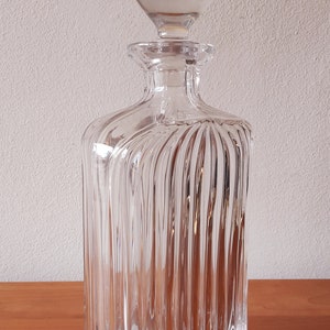 Puede incluir: Una decantador de vidrio transparente con un tap&oacute;n redondo. La decantador tiene un cuerpo cuadrado con nervaduras verticales.