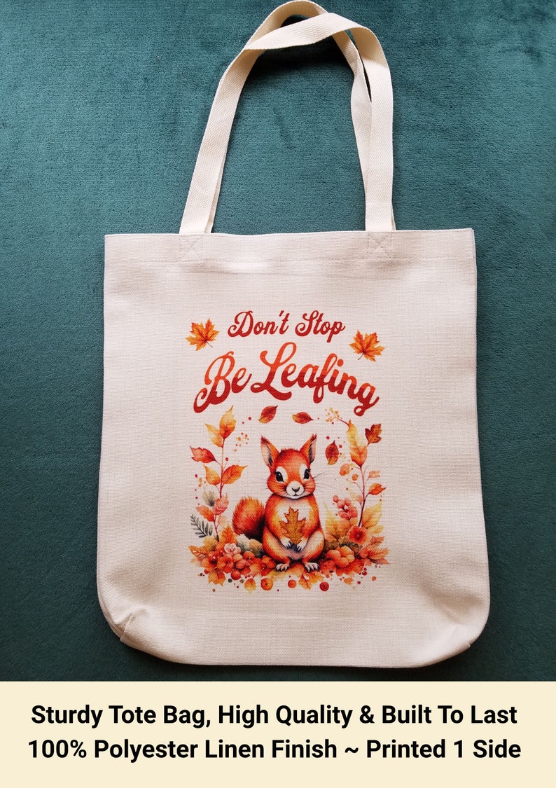 May include: A white tote bag with a squirrel and autumn leaves printed on it. The text "Don't Stop Be Leafing" is printed in red on the bag. The bag is made of 100% polyester linen and is printed on one side.