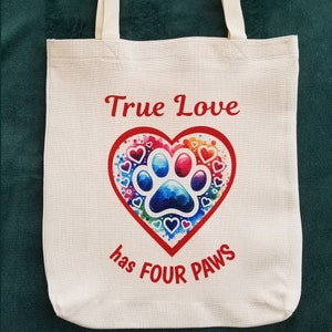 May include: A white canvas tote bag with red text that reads "True Love has Four Paws". The bag features a colorful heart with a paw print inside and smaller hearts surrounding it.