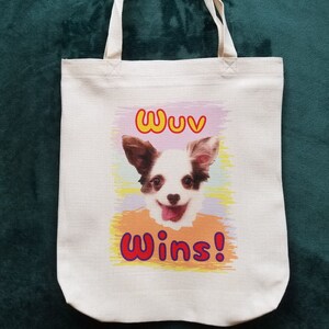 K&ouml;nnte beinhalten: Cremefarbene Tragetasche mit einem l&auml;chelnden Hunde-Motiv. Der Text "Wuv Wins!" ist &uuml;ber und unter dem Hund aufgedruckt. Die Tasche hat eine rechteckige Form und zwei Henkel.