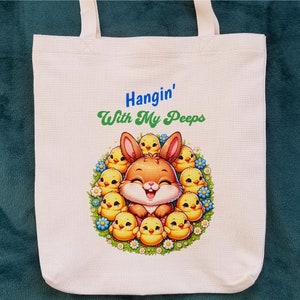 May include: A white canvas tote bag with a cartoon bunny surrounded by yellow chicks. The text "Hangin' With My Peeps" is printed on the bag.
