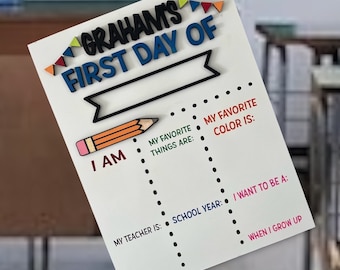 May include: White board with the text "GRAHAMS FIRST DAY OF" in colorful letters. The board has a pencil icon and dotted lines for writing in information such as "I am", "My favorite things are", "My favorite color is", "My teacher is", "School year", "I want to be a", and "When I grow up".
