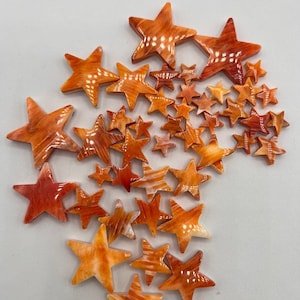 May include: A collection of orange and white star-shaped shell cabochons. The cabochons are various sizes and have a natural, organic look.