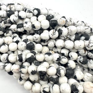 May include: A close-up of a strand of white and black round beads. The beads have a speckled pattern of black and grey on a white base. The beads are approximately 0.8 cm in diameter and are strung together.