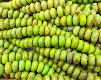 May include: A collection of round, disc-shaped beads in various shades of lime green and olive green. Each bead features natural brown veining and a smooth, polished finish. The beads are strung together on thin white thread in multiple rows.