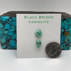 May include: Two pieces of green variscite gemstone, one round and one teardrop shaped, on a white card with the text "BLACK BRIDGE VARISCITE". A US quarter is shown for scale.