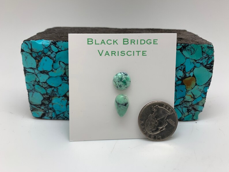 May include: Two pieces of green variscite gemstone, one round and one teardrop shaped, on a white card with the text "BLACK BRIDGE VARISCITE". A US quarter is shown for scale.