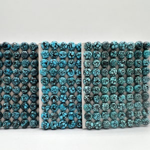 May include: A close-up of three rows of turquoise cabochons, each row containing 12 cabochons. The cabochons are a light blue color with black matrix.