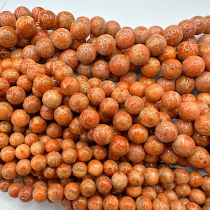 May include: Close-up of a collection of orange-colored, round beads. The beads have a speckled texture and vary slightly in size. They are strung together, suggesting they are for jewelry making or crafting.