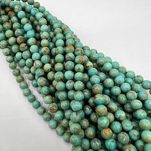 May include: A strand of turquoise blue beads with brown and gold marbling. The beads are round and smooth, and they are strung together on a clear thread.