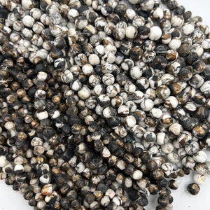 May include: A strand of white, black, and gold speckled beads. The beads are round and have a natural, organic look.
