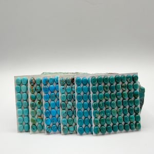 Puede incluir: Una colección de piedras preciosas de turquesa en varios tonos de azul y verde. Las piedras preciosas de forma ovalada están dispuestas en filas ordenadas sobre láminas de plástico transparente. Las piedras varían en color de azul claro a verde azulado intenso.