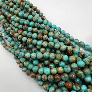 May include: A strand of turquoise blue and brown round beads. The beads have a marbled pattern and are arranged in a pile.