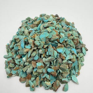 May include: A large pile of small, irregular turquoise stone chips. The stones feature a vibrant cyan-blue color with natural brown matrix inclusions and rough, jagged edges, creating a textured appearance across the entire collection of pieces.