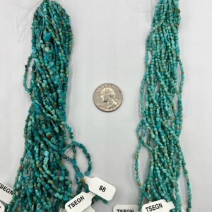 May include: Two strands of turquoise beads, labelled #5 and #6, are displayed on a white surface. The beads are a light blue-green colour and are approximately 6 mm in diameter. The strands are about 45 cm long and are arranged in a vertical orientation. The beads are strung on a thin wire and are separated by small gaps. The beads are a popular material for jewellery making.