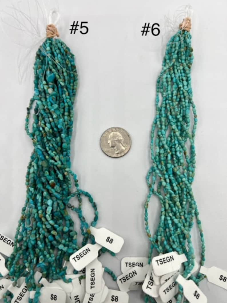 May include: Two strands of turquoise beads, labelled #5 and #6, are displayed on a white surface. The beads are a light blue-green colour and are approximately 6 mm in diameter. The strands are about 45 cm long and are arranged in a vertical orientation. The beads are strung on a thin wire and are separated by small gaps. The beads are a popular material for jewellery making.