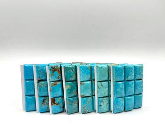 May include: A set of nine turquoise cabochons, each with a unique pattern of blue and brown, are arranged in three rows of three. The cabochons are mounted on white backing cards.