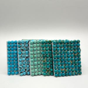 May include: Five rectangular cards each featuring a grid of small, round turquoise beads. The beads vary in color from light sky blue to deep teal, with some displaying natural dark matrix patterns and others showing a solid, uniform color.